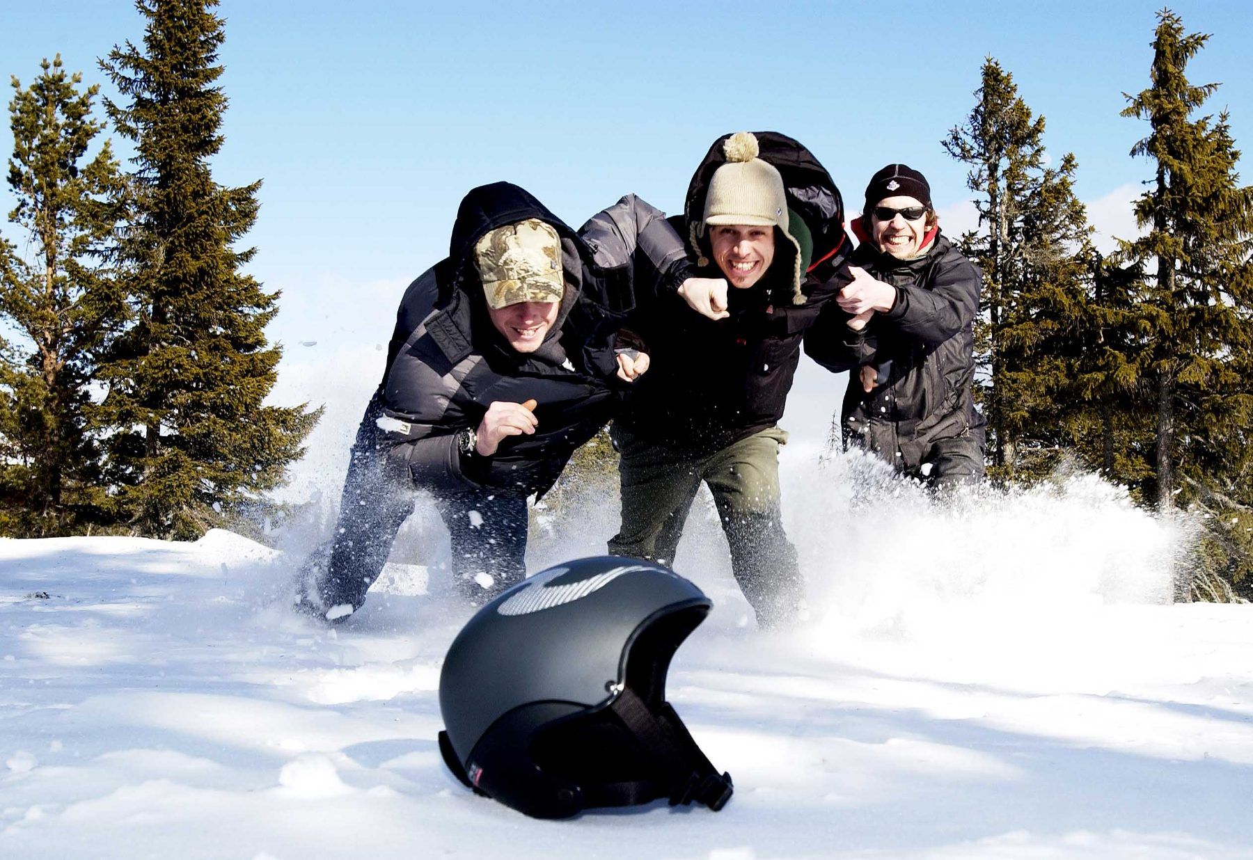 Three friends charging through snow with a black helmet in the foreground