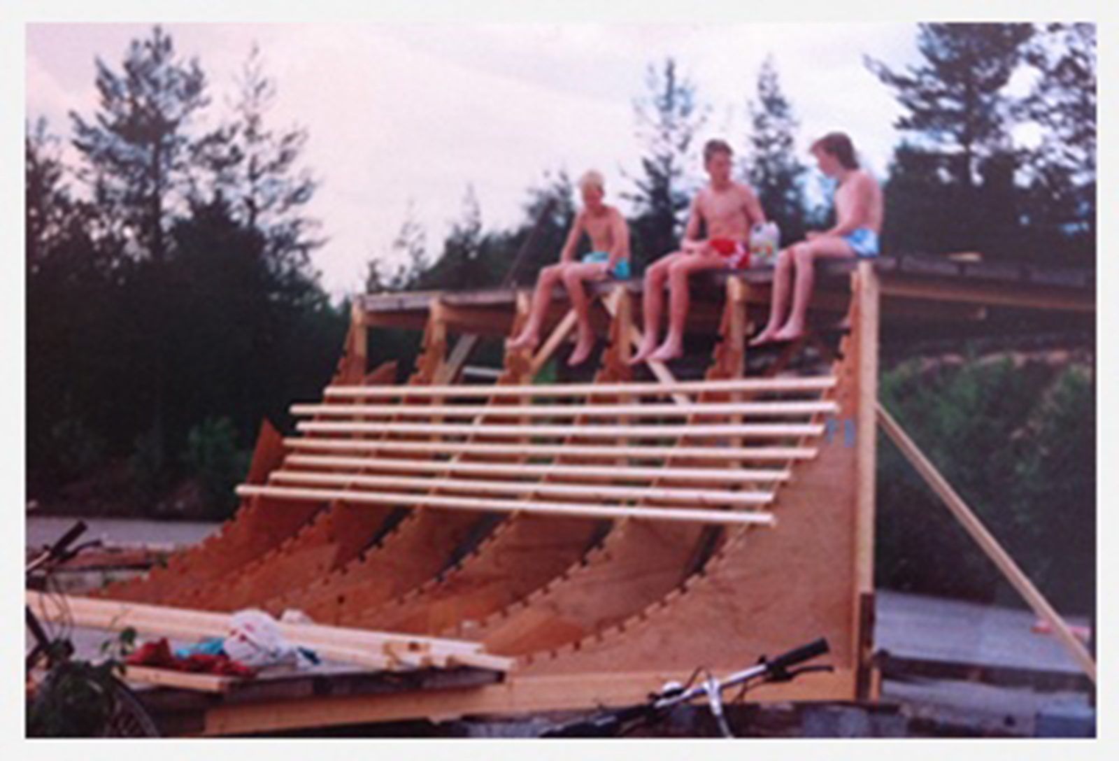 Three friends sitting on top of a homemade halfpipe in the forest