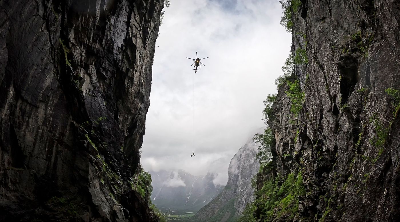 Rescue helicopter hoisting a crew member in a mountain gorge